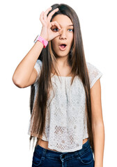 Young brunette girl with long hair wearing white shirt doing ok gesture shocked with surprised face, eye looking through fingers. unbelieving expression.