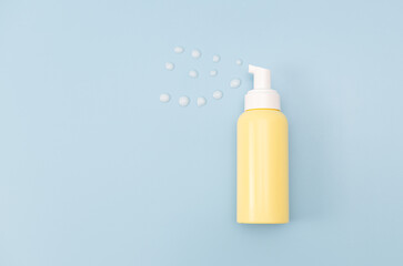 Yellow bottle with dispenser and drops of gel on a blue background.