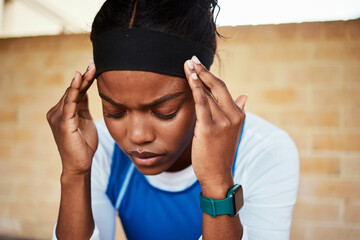 Fitness, headache and black woman in pain during run, exercise or workout against brick wall background. Sports, migraine and girl suffering with ache, discomfort and fatigue during cardio routine