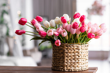 Bright, colorful tulips in a wicker basket on a wooden table in the living room