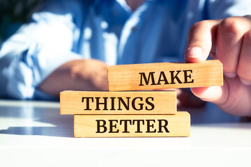 Close up on businessman holding a wooden block with "MAKE THINGS BETTER" message