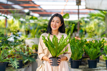 Portrait of Happy Asian woman holding potted plant in front of plant shop street market on summer vacation. Attractive woman enjoy hobbies and leisure activity growing plant and flower at home.