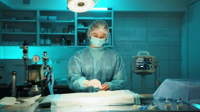 Nurse prepares for the medical prosedure by puting on surgical gloves. She is in the surgery room alone and is prepearing the work space and herself High quality 4k footage