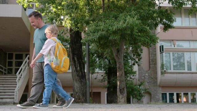 An elementary school student walks from school accompanied by his middle-aged father. A boy tells his dad how his school day went on the first day after the holidays. Primary school pupil with parents