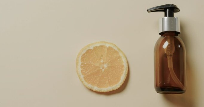 Close up of glass bottle with pump, lemon slice and copy space on beige background