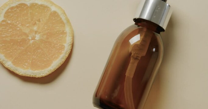 Close up of glass bottle with pump, lemon slice and copy space on beige background