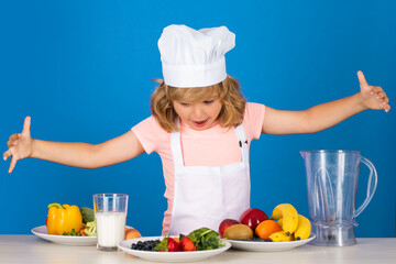 Cooking children. Fruits and vegetables for kids. Chef kid boy making fresh vegetables for healthy eat. Portrait of little child in form of cook isolated on grey background. Kid chef. Cooking process.