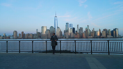 Guy standing at the waterfront in Jersey City and watching the skyline of Manhattan - drone photography