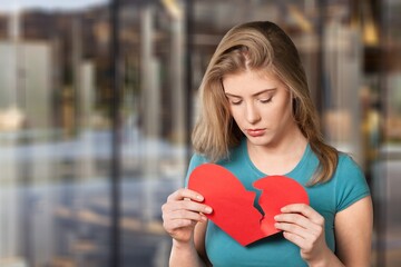 Young unhappy woman with broken heart made from paper