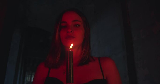 Attractive with style woman hold burning candle in dark, lit by red neon light