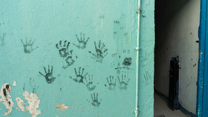 Blue green turquoise wall with black handprints and a vertical pipe with a door in the right side