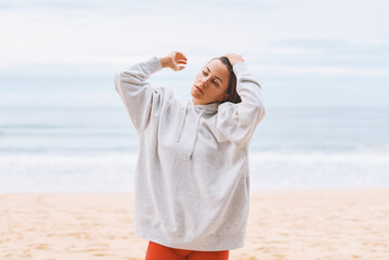 Attractive young woman in white hoodie walking along the seashore early morning