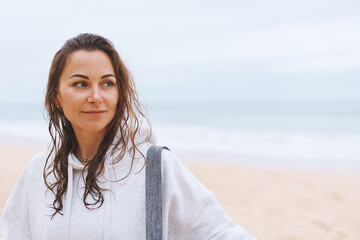 Close up portrait young woman in hoodie walking along the seashore going to do yoga on sand beach - 576552778