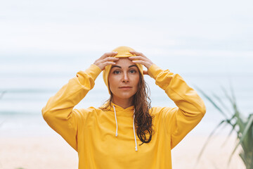Young woman in yellow hoodie, yellow hat standing on seashore in a relaxed state. Tropical view