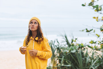 Young woman in yellow hoodie, yellow hat standing on seashore in a relaxed state. Tropical view