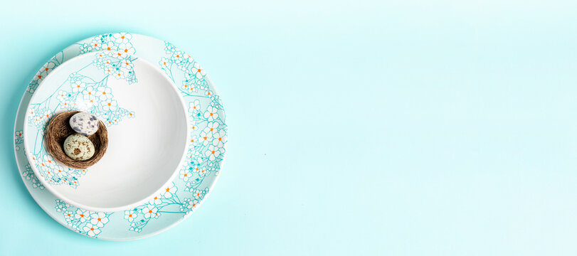 Nest with quail eggs on plates with floral pattern on light blue. Easter banner. Top view Copy space