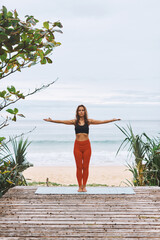Attractive young athletic woman in black sport bra, red pants doing yoga exercises in front of sea