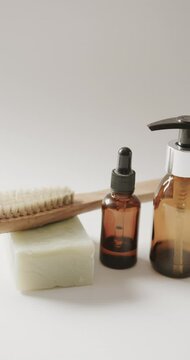 Vertical video of close up of glass bottles, soap and brush and copy space on beige background