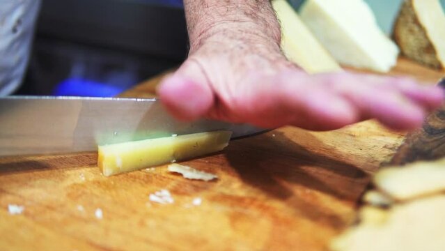 Shot of a person cutting cheese with a knife on a wooden board in slow motion.