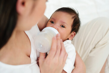 mother feeding milk bottle to her newborn baby on bed