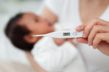 mother measuring temperature of her ill baby. sick child with high fever on bed