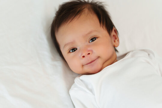 happy newborn baby smilling while lying on a bed