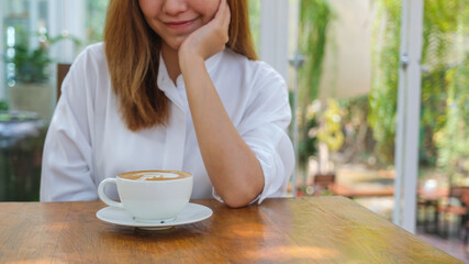 Closeup image of a young woman looking at a cup of hot coffee in cafe