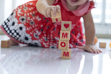 Close up hands of child baby girl play wooden block, try stacking wooden cube blocks on floor, letter M, O, M, on block, selective focus