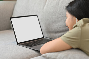 Carefree young woman lying on comfortable sofa and surfing internet on laptop.