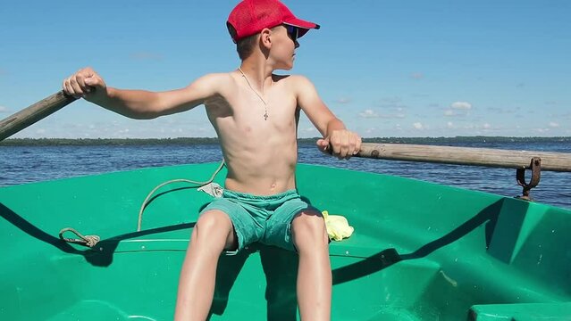 The boy is 12 years old rowing the oars, sailing the boat on the river. The concept of a summer vacation.