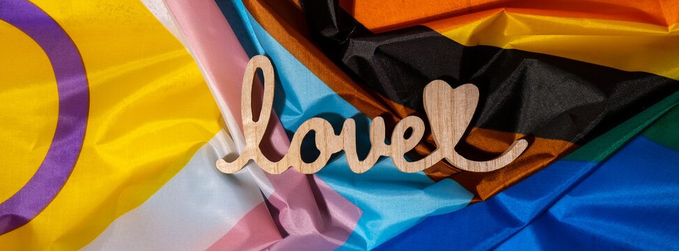 Banner Wooden word love with heart romance on Rainbow LGBTQIA flag made from silk material. Valentine's Day greeting card. Symbol of LGBTQ pride month. Equal rights. Peace and freedom. Support LGBTQIA