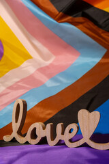 Wooden word love with heart romance on Rainbow LGBTQIA flag made from silk material. Valentine's...