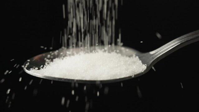 spoonful of sugar food pile sugar.sugar fall on spoon.slow fall sugar.sweet ingredient on black