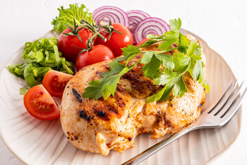 grilled chicken breasts on a white ceramics plate serving with parsley, tomato slices. close-up. diet food.