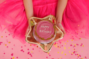 Child girl in a pink dress holds a delicious sweet bento cake with the inscription happy birthday