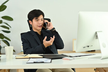 Millennial male business executive looking at laptop computer screen, discussing project on mobile phone