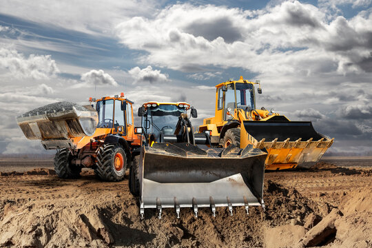 Bulldozer or loader moves the earth at the construction site against the blue sky. An earthmoving machine is leveling the site. Construction heavy equipment for earthworks.