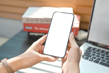 Woman hands holding smart phone front of laptop computer at her workplace. Close up view