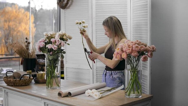 A young beautiful woman engaged in floristry begins to collect the best flowers for her flower arrangement. A girl cuts thorns on roses with a pruner. Floristry