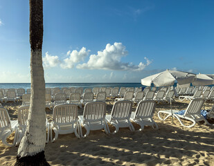 Beach chairs on white sand beach with blue sky and sun.
