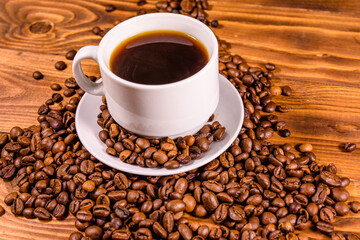 Cup of hot coffee and scattered coffee beans on wooden table