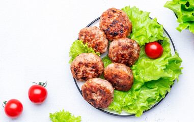 Homemade fried pork and beef meatballs with green lettuce and tomatoes, white table background, top view