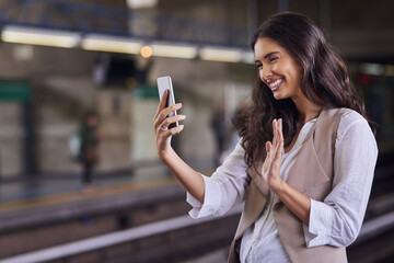 Saying hello to the people at home. Cropped shot of a young attractive woman video calling with her cellphone while commuting with the train. - obrazy, fototapety, plakaty