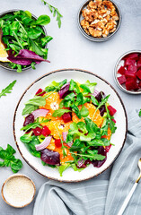 Beet and orange healthy salad with arugula, lamb lettuce, red onion, walnut and tangerine, gray kitchen table. Fresh useful vegan dish for healthy eating