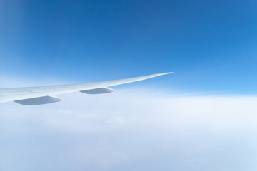 Wing of an airplane jet flying above clouds with blue sky from the window in traveling and transportation concept. Nature landscape background.