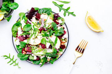 Beet, feta cheese and pear healthy salad with arugula, lamb lettuce, red onion, chard and walnut, white kitchen table. Fresh delicious dish for healthy eating