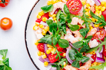 Delicious shrimp salad with sweet corn, cherry tomatoes, lamb lettuce and red onion on white table background. Top view