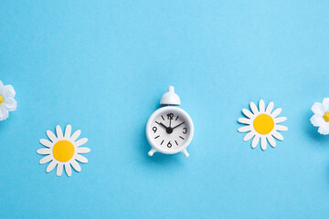 White Alarm Clock and Spring Daisy Flowers on Blue Background