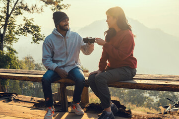 Happy traveler couple resting on mountains in sunrise with drinking coffee - obrazy, fototapety, plakaty