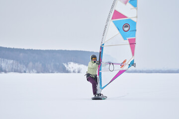 A middle-aged woman, a snowsurfer, rides a sailboard. Snowsurfing on a cloudy winter day.